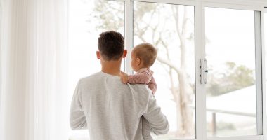 Man Holding A Baby Looking Out Window