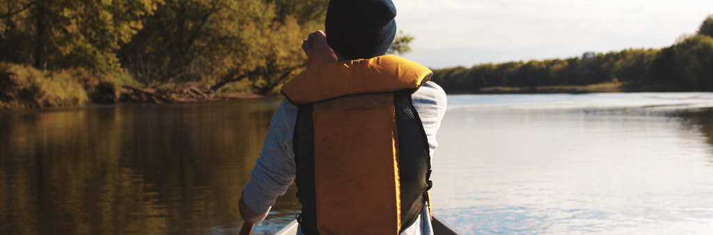 Person With Yellow Life Jacket And Black Knit Hat In A Boat On Water