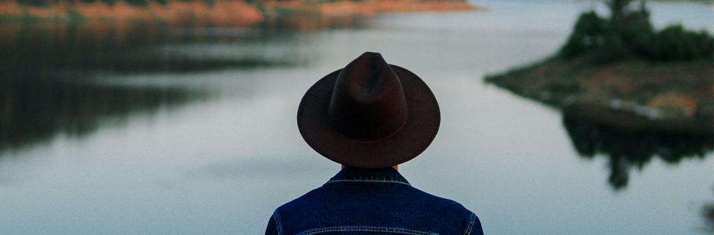 Man In Jean Jacket And Black Cowboy Hat Facing The Water