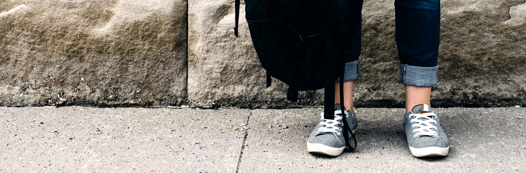 Woman With Blue Tennis Shoes Holding Black Backpack On Concrete Sidewalk