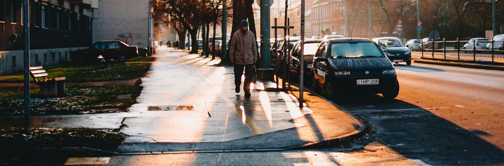 Man Walking On Sidewalk With Sun Shining